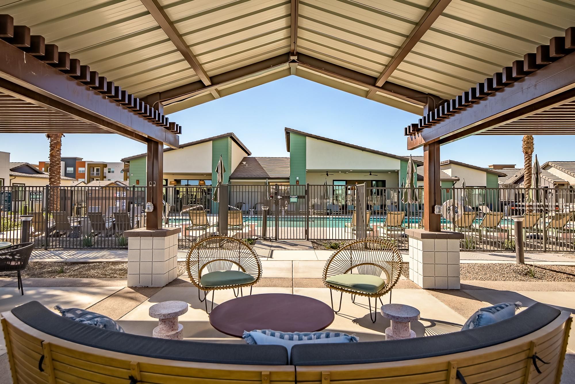 Sonita apartments Outdoor patio seating under a pergola with a view of a fenced swimming pool and modern buildings.