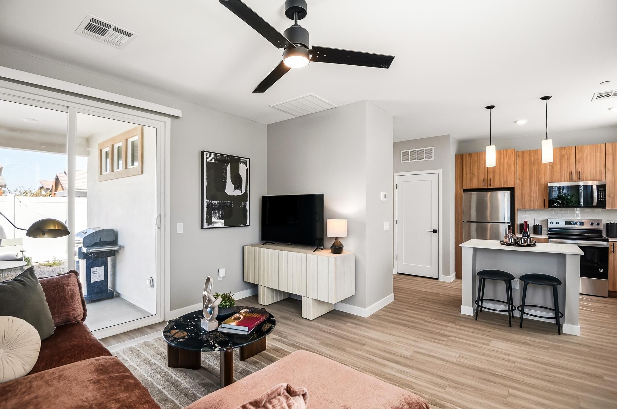 Sonita apartments Modern living room with a TV, stylish furniture, and open kitchen; glass door leads to a patio with a grill.