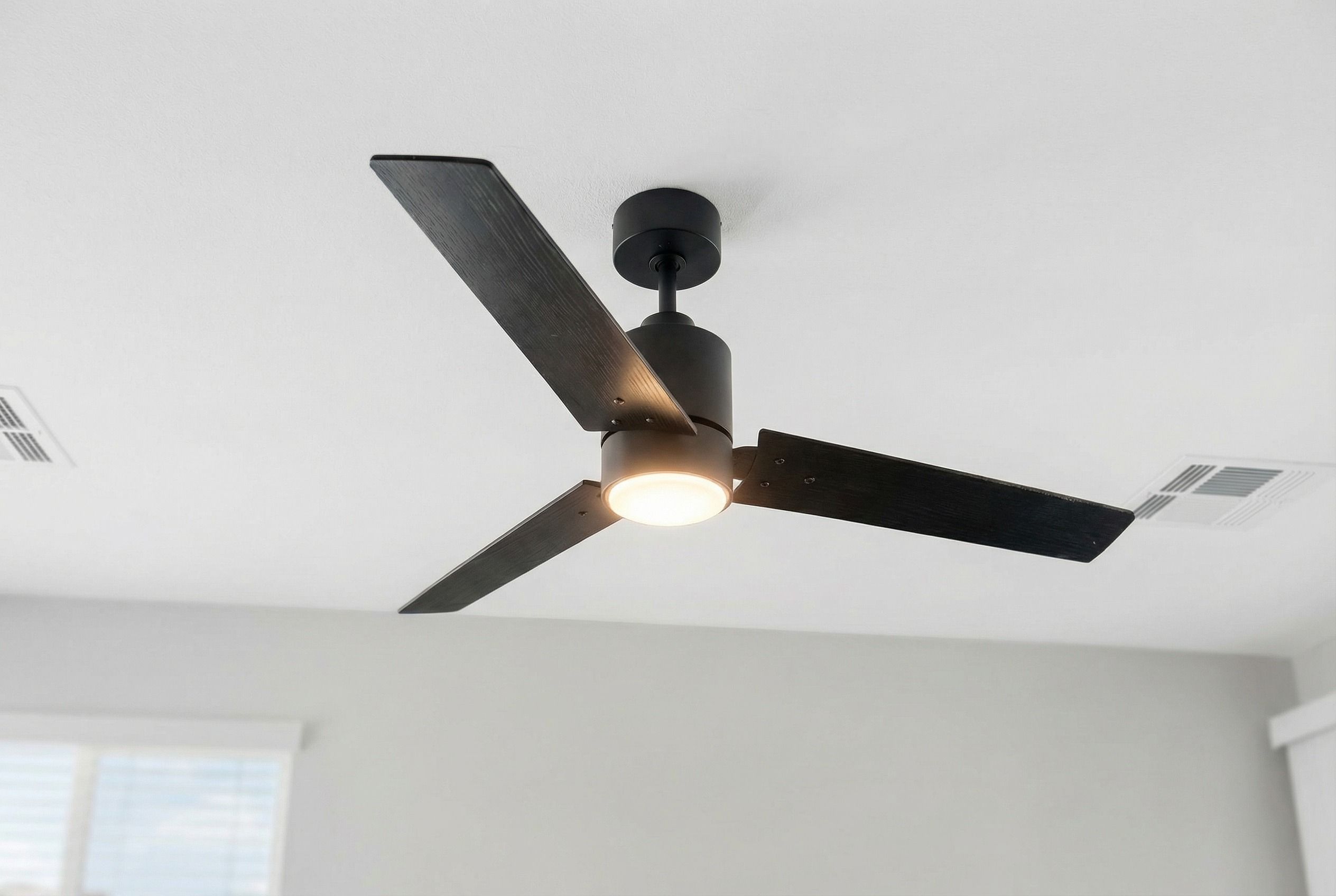 A modern black ceiling fan with three blades and a light, mounted on a white ceiling.