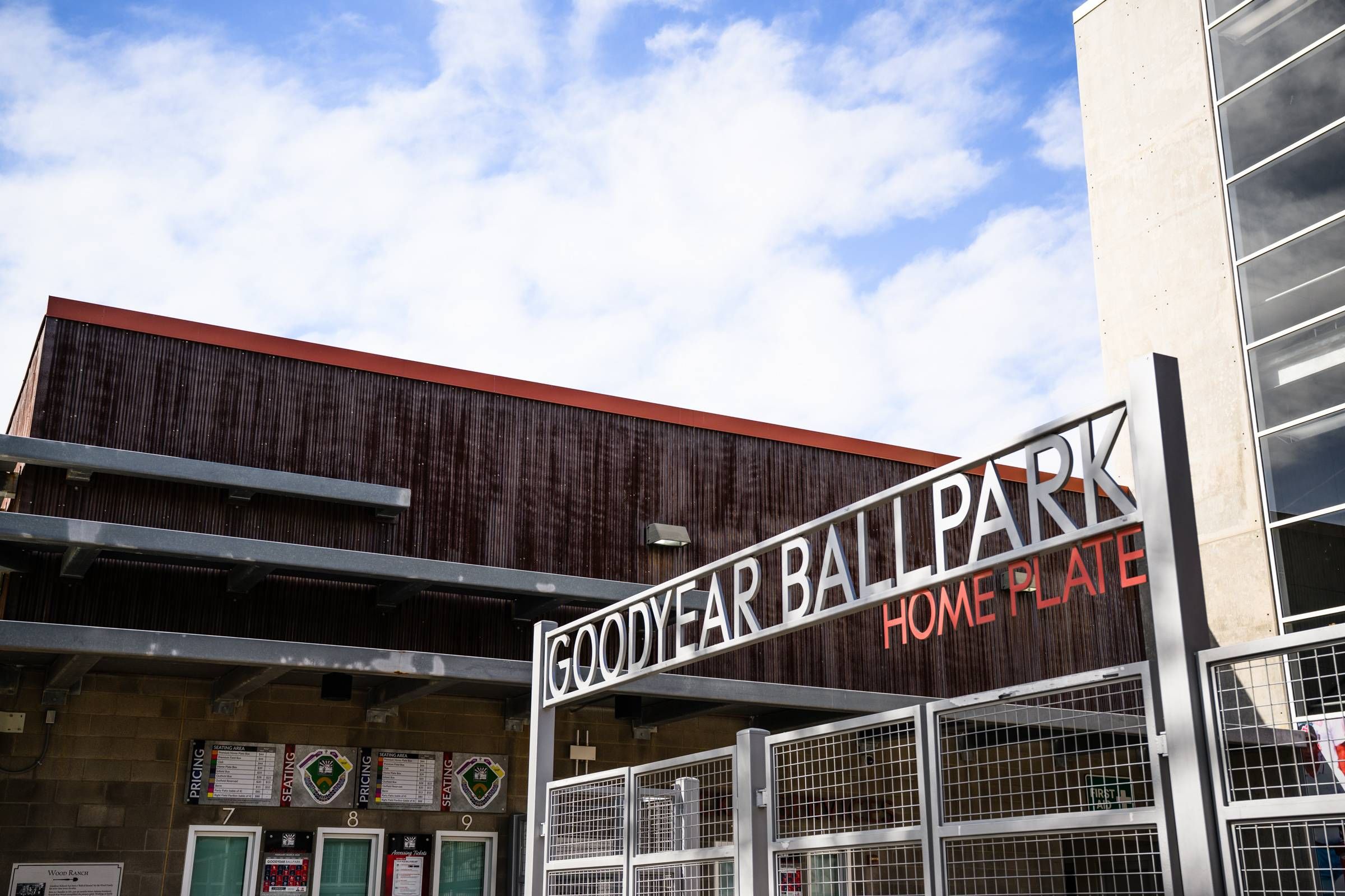 Goodyear Ballpark entrance with "Home Plate" sign, ticket windows, and partly cloudy sky above.