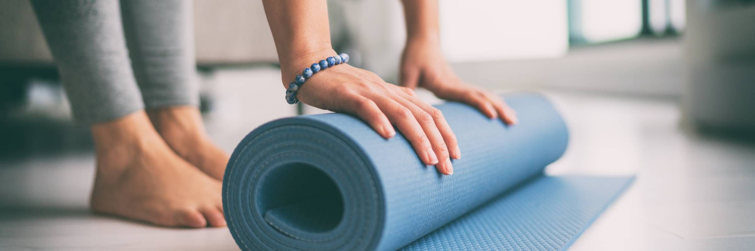 Sonita apartments Person rolling up a blue yoga mat on the floor, with bare feet and a beaded bracelet visible.