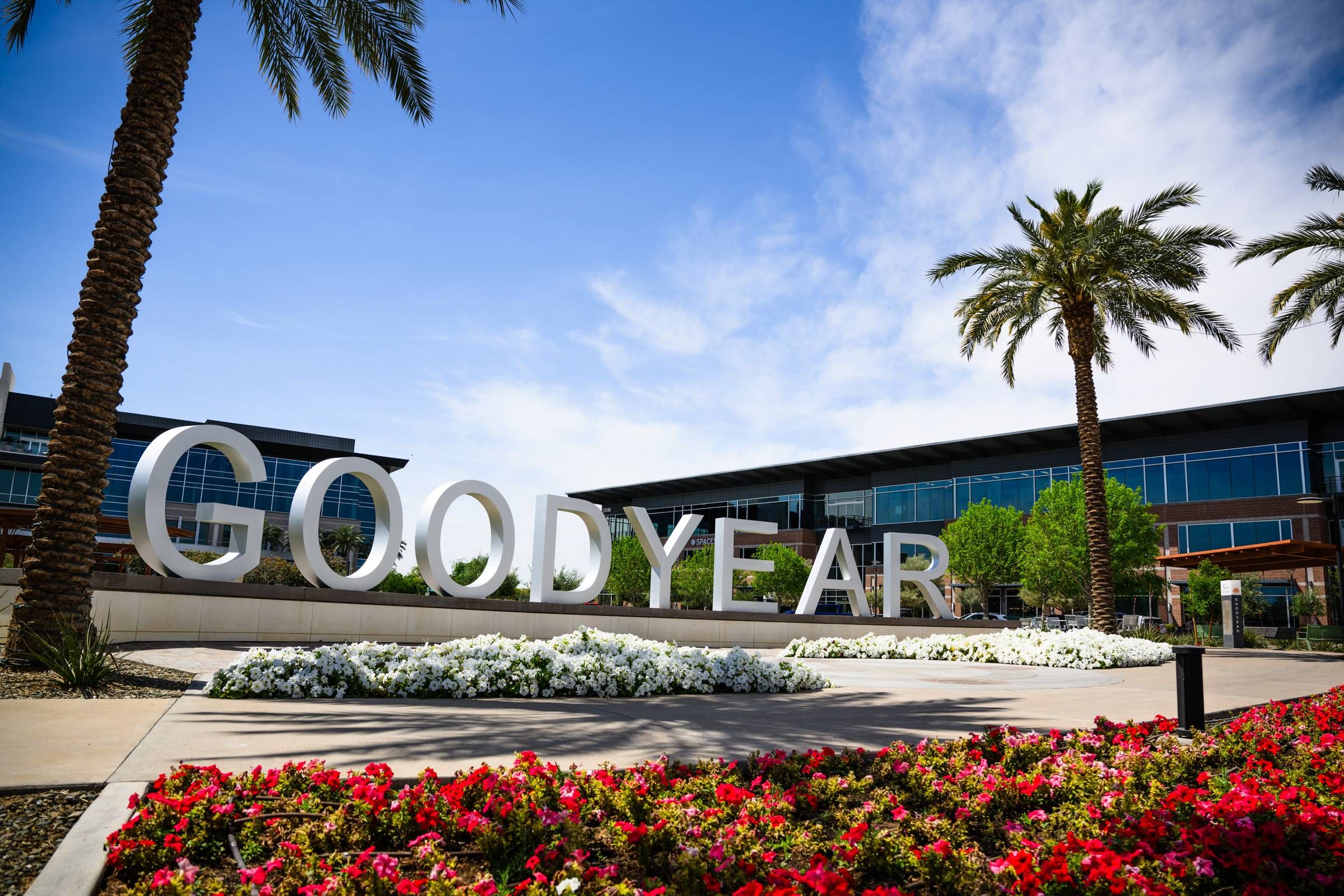 Large "GOODYEAR" sign surrounded by flowers and palm trees in front of modern buildings on a sunny day in Goodyear, AZ near Sonita Apartments.