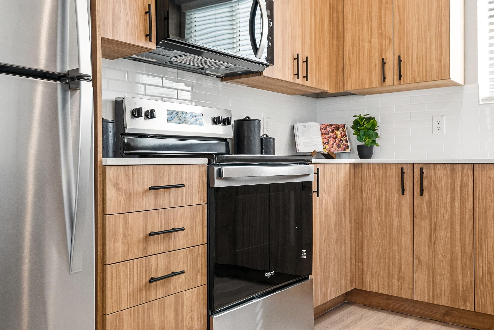 Sonita apartments Modern kitchen with wood cabinets, stainless steel appliances, and white tile backsplash.