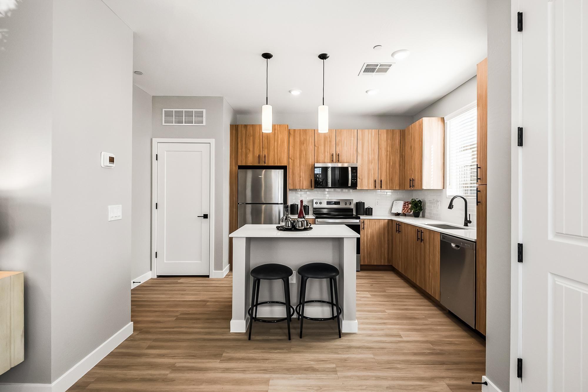 Sonita apartments Modern kitchen with wood cabinets, stainless steel appliances, island with two stools, and pendant lights.