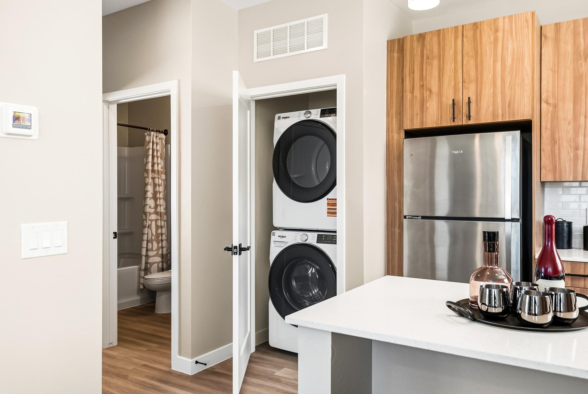 Sonita apartments Modern kitchen with a stacked washer and dryer in a closet, and a view into a bathroom with a shower curtain.