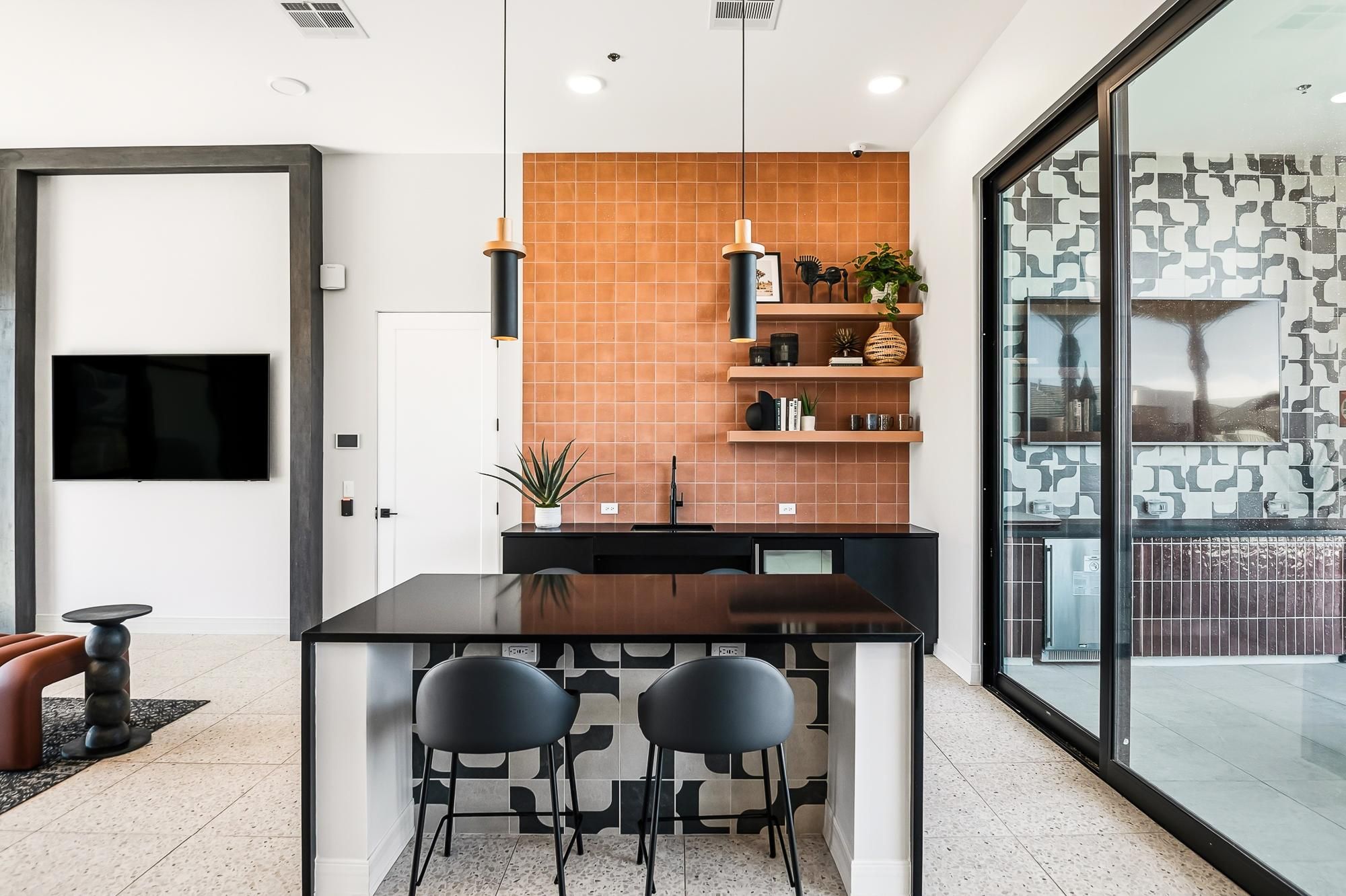 Sonita apartments Modern kitchen with orange tile backsplash, black countertops, two black chairs, and open shelves with decor.