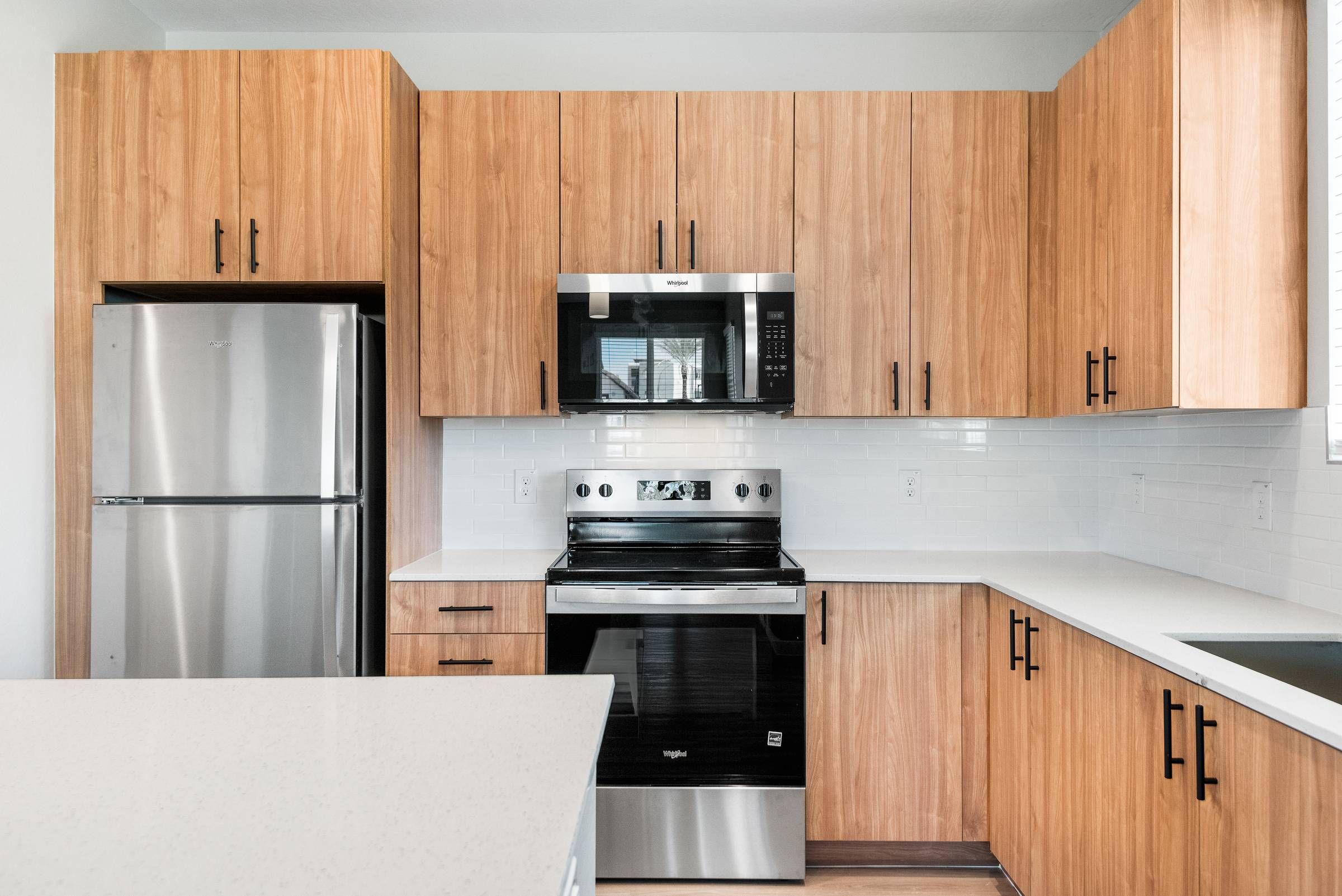 Sonita Apartments in Goodyear, AZ Modern kitchen with wood cabinets, stainless steel fridge and oven, white countertops, and a microwave.