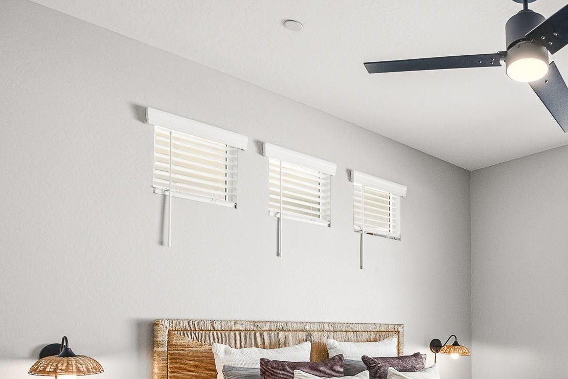 Sonita apartments Bedroom with three small windows, white blinds, ceiling fan, wicker headboard, pillows, and wall lamps.