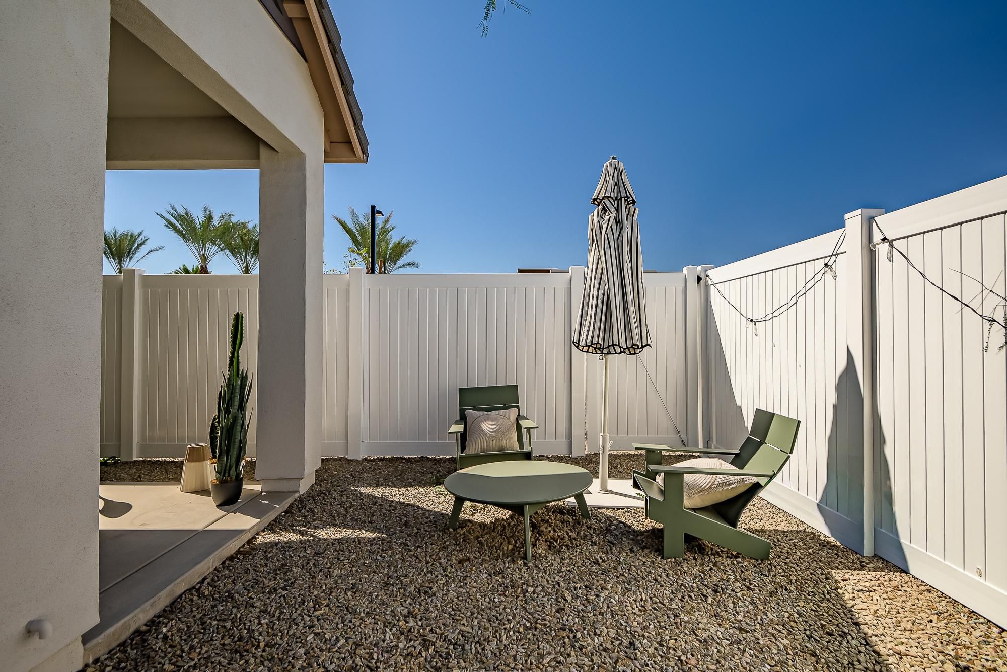 Sonita apartments Small patio with green chairs, round table, closed umbrella, cactus, and string lights against a white fence.