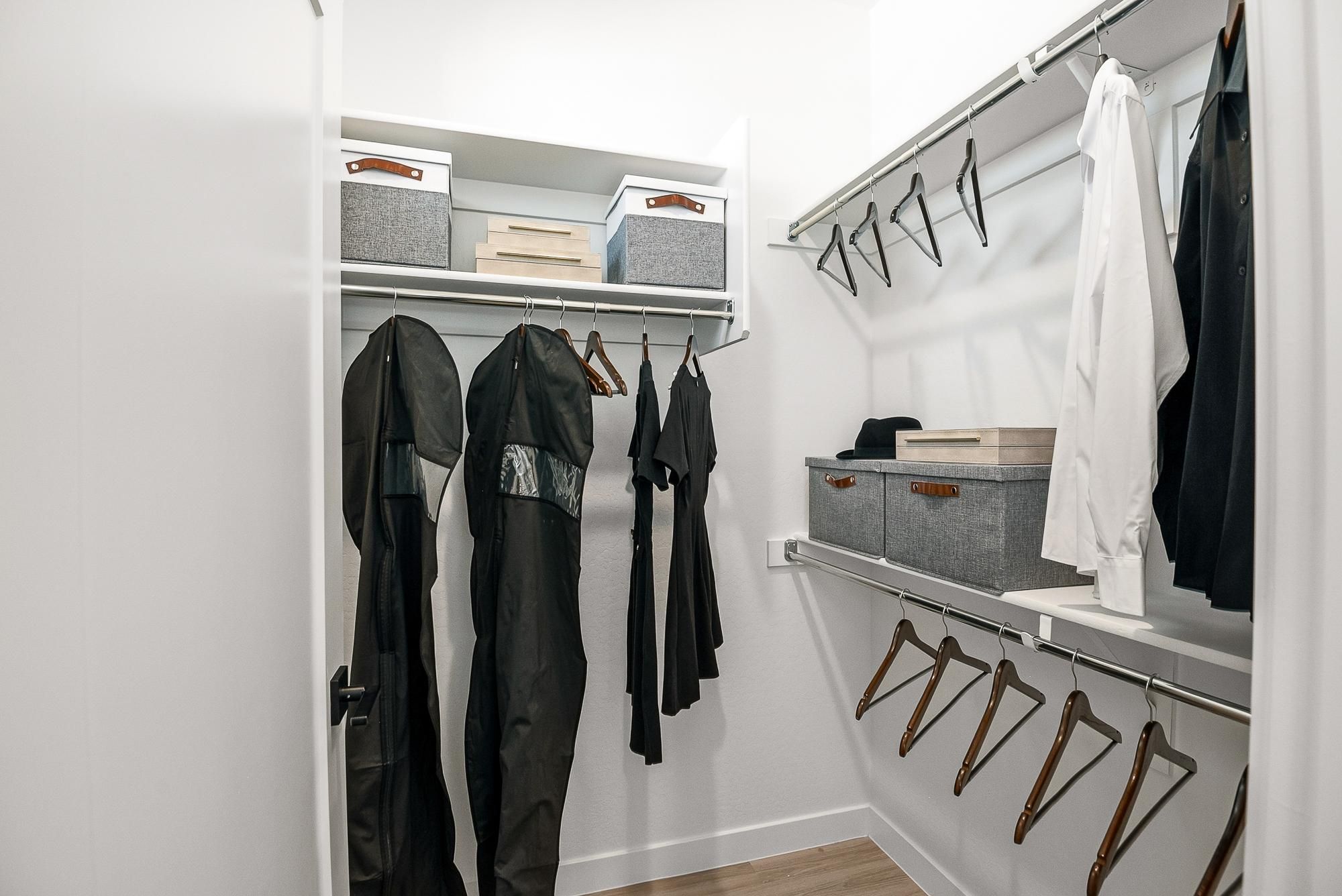 Sonita apartments Modern walk-in closet with hanging clothes, empty wooden hangers, storage boxes, and white shelves.