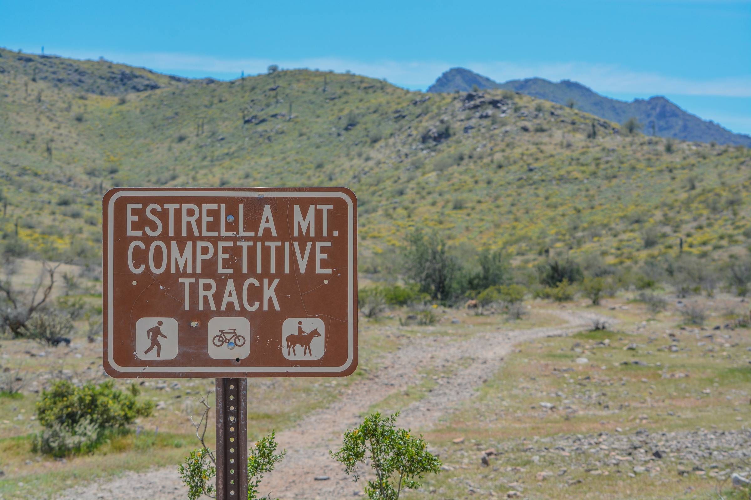 Sign for Estrella Mountain Competitive Track with icons for hiking, biking, and horseback riding; desert hills in background.