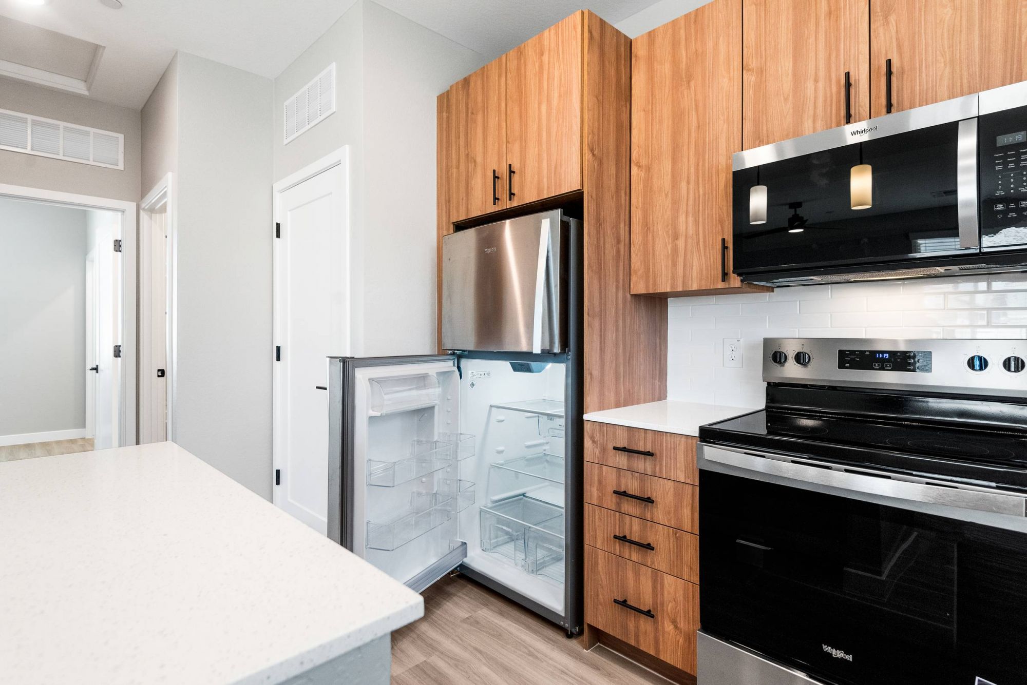 Sonita Modern kitchen with wood cabinets, an open stainless steel fridge, and a black oven under a microwave.