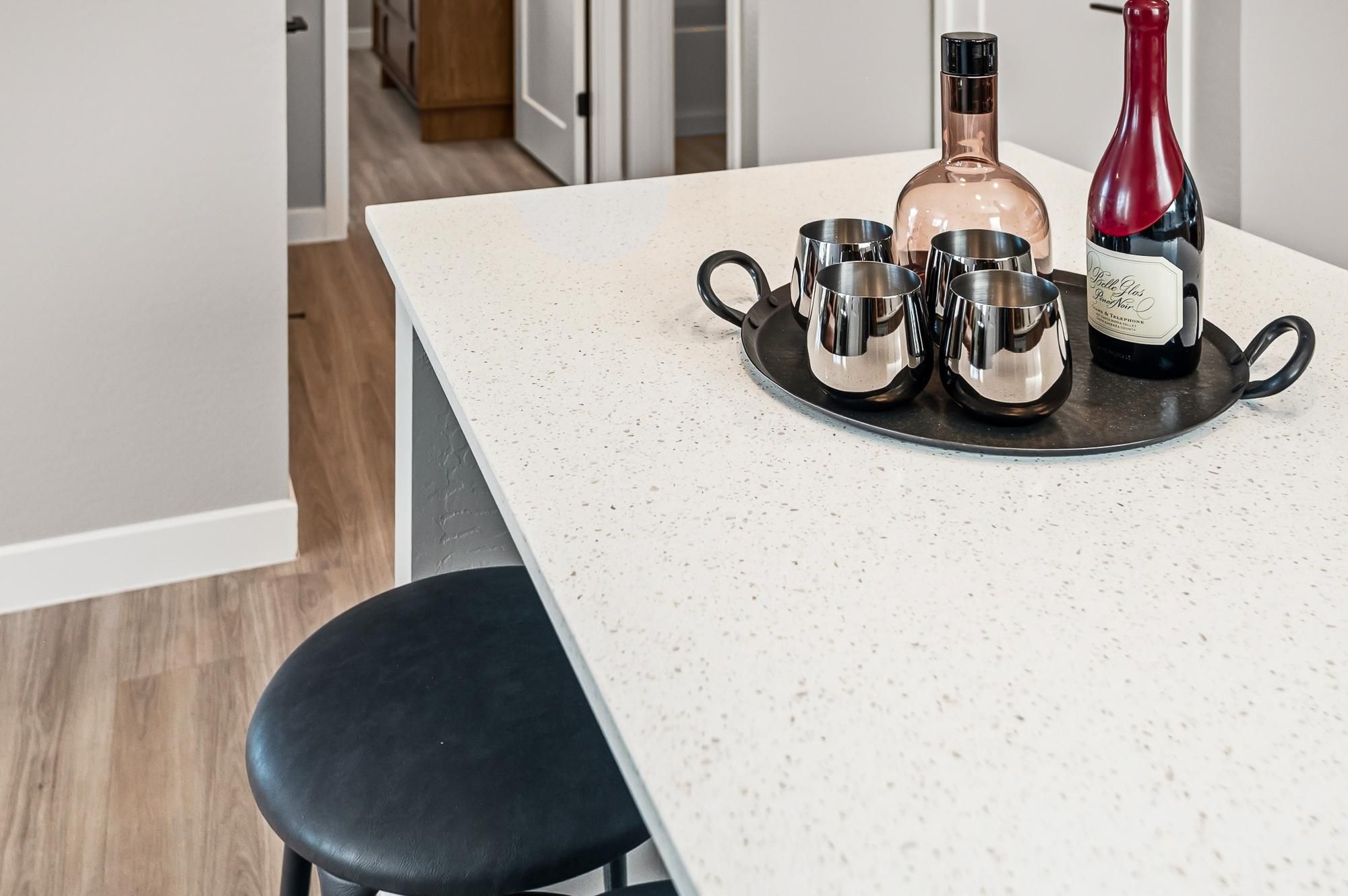 Sonita apartments White kitchen island with a black tray holding mugs and bottles, next to a black stool on wood flooring.