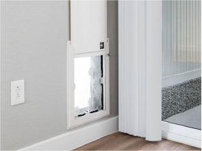Sonita White pet door installed in a wall next to an electric outlet and a glass sliding door.