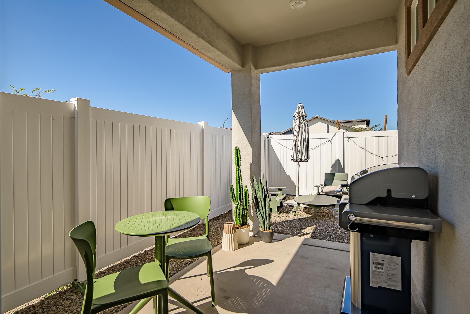 Sonita apartments Small patio with green chairs, table, BBQ grill, potted cactus, white fence, and outdoor umbrella.